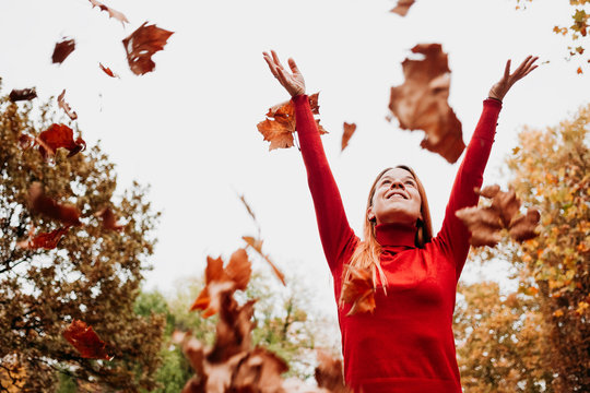 Young Woman Throwing Autumn Leaves In The Air In The Park