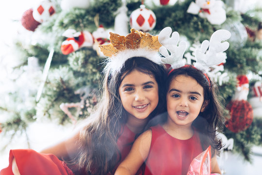 Christmas and New Year. Young girls in festive costumes at home sitting under the christmas tree laughing happy close-up