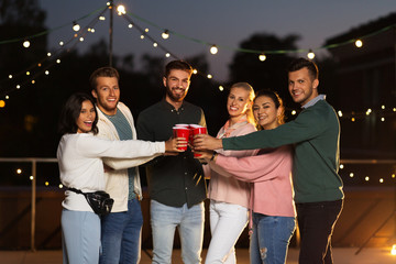 leisure, celebration and people concept - happy friends with drinks toasting at rooftop party at night