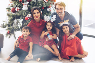 Christmas and New Year. Family of five at home sitting under christmas tree hugging smiling cheerful together