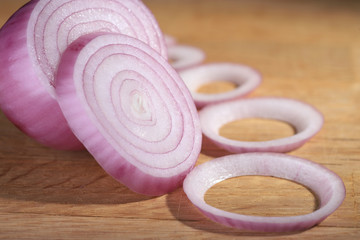 Obraz na płótnie Canvas Red onion or Allium cepa half cut and sliced on a wooden cutting board