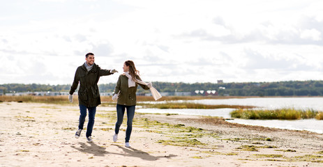 love, relationship and people concept - smiling couple running along autumn beach and holding hands