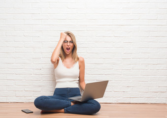 Beautiful young woman sitting on the floor working using laptop at home annoyed and frustrated shouting with anger, crazy and yelling with raised hand, anger concept