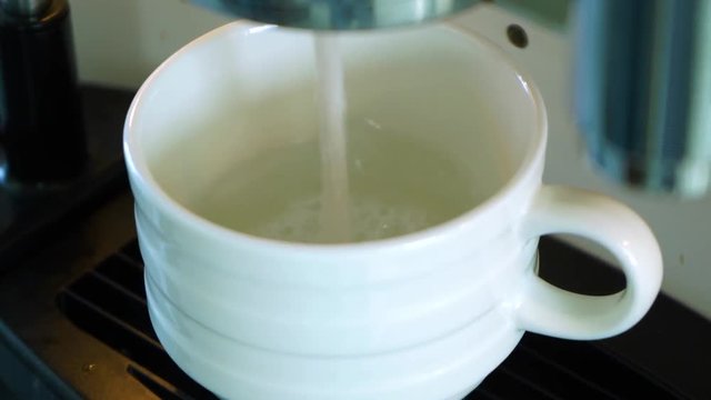 Hot white milk pouring into white cup from not working properly automatic coffee machine. Real time full hd video footage.