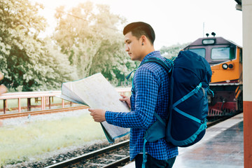Asian man holding map paper and looking router with plan for travel at train station.