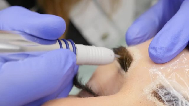Young beautiful woman getting eyebrows tattoo. permanent makeup for eyebrows at beauty salon. 4K