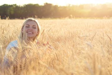 Portrait of a young woman in a wheat field,touches the golden spikelet.