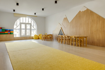playing room interior with wooden chairs and tables, yellow carpet, bean bag chairs and bright...