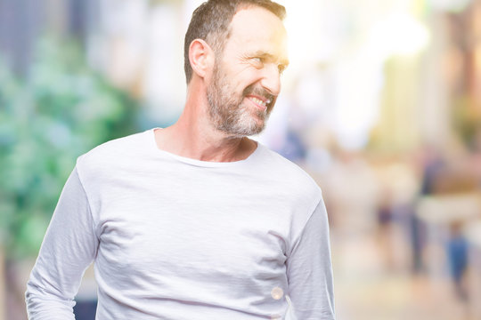 Middle age hoary senior man wearing white t-shirt over isolated background looking away to side with smile on face, natural expression. Laughing confident.