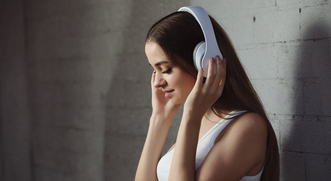 Young woman listening to music with headphones near wall