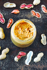 Peanut butter in a jar. Peanuts in the shell. Peanut butter and peanuts on a dark, scuffed surface.