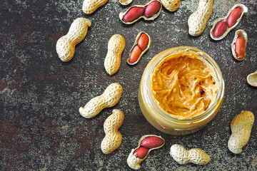 Peanut butter in a jar. Peanuts in the shell. Peanut butter and peanuts on a dark, scuffed surface.