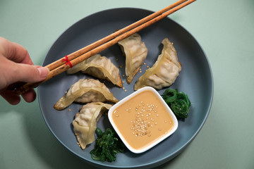 Frau isst gebratene asiatische Dim Sum Teigtaschen mit Wakame Algen Salat und Sesam Soße auf...