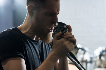 Side view portrait of handsome bearded man singing to microphone during band performance on stage,...
