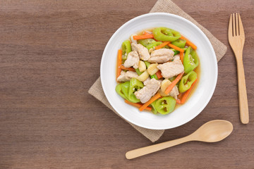 top view of stir fried pork with banana pepper in a ceramic dish on wooden table. hot and spicy homemade style food concept.