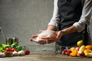 The chef holds a raw chicken in his hands against the background with vegetables, for a holiday, Christmas, New Year, Benefit Day. Background for the menu and for the book of cooking recipes