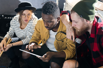 Portrait of three young people using digital tablet while writing music in band rehearsal