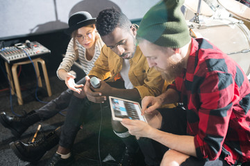 High angle portrait of three young people using digital tablet while writing music in band rehearsal