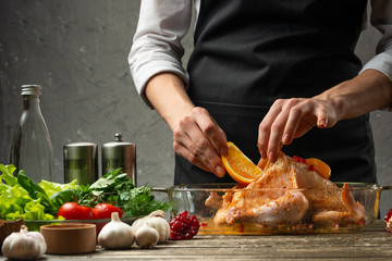The chef prepares chicken with fruit for baking for a holiday, against the background of a concrete wall. Background for the menu and for cooking recipes