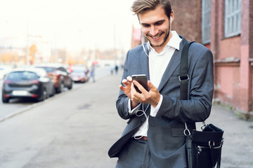 Happy attractive young businessman walking and using mobile phone outdoors.