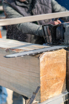 cropped image of carpenter in protective gloves using machine saw at sawmill. Wooden log being cut with chainsaw. vertical photo