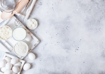 Fresh dairy products on white table background. Glass of milk, bowl of flour and cottage cheese and eggs. Box of baking utensils. whisk and spatula in vintage wooden box.Top view. Space for text