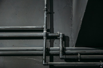 Black pipes on dark wall background as abstract industrial pipeline texture