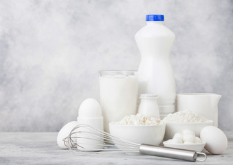Fototapeta na wymiar Fresh dairy products on white table background. Plastic bottle and glass of milk, bowl of cottage cheese and baking flour and mozzarella. Eggs and cheese. Steel whisk.