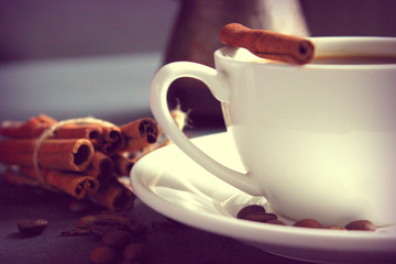 Close-up of a white Cup of coffee with cinnamon sticks and scattered coffee beans on the coffee table