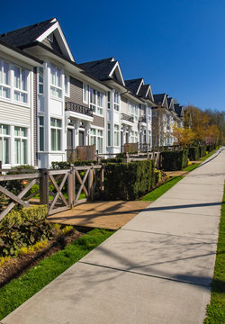 Row of new townhomes in a sidewalk neighborhood. On a sunny day in spring against bright blue sky.