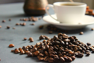 Close-up of a bunch of coffee beans scattered on the table, a white Cup and saucer and a coffee Turk , selective focus.copy space