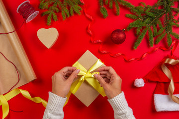 Christmas gift wrapping. Woman's hands packing Christmas present box on red table background
