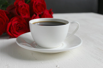 A Cup of coffee, a bouquet of red roses and a gift with a red ribbon on the table close-up. Valentine's day, birthday concept.