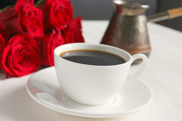 Obraz na płótnie Canvas Black coffee in a white Cup with a saucer on the table, a bouquet of red roses. Cafe, restaurant, coffee with your loved one, a beautiful bouquet.Top view