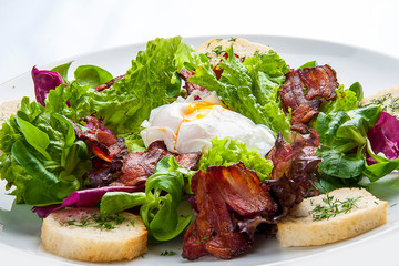 Salad with bacon and poached egg on a white plate