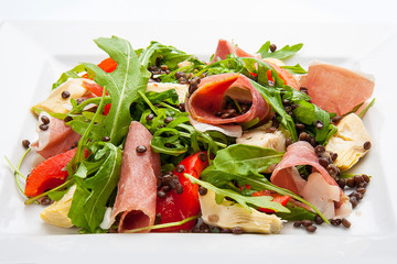 Salad with prosciutto and artichokes on a white plate