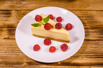 White plate with cheesecake New York, leaf of mint and raspberries on wooden table