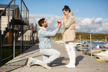 Serious handsome young man in love standing on one knee and holding open jewelry box while...