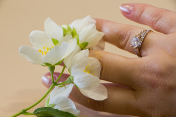 Obraz na płótnie Canvas Engagement ring on hand and jasmine flowers on pink wooden background