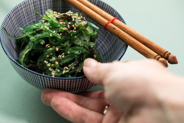 Frau isst Japanischen Wakame Algen Salat und Sesam mit Stäbchen