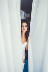 Fototapeta premium gentle portrait of a curly woman in white lingerie on a background of curtains