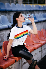 Image of sporty disabled invalid sportswoman in tracksuit wearing prosthesis sitting on floor in...