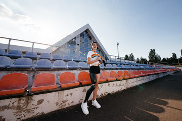 Photo of athletic disabled girl with bionic leg in sportswear standing and smiling outdoor over...