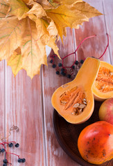 Fall vegetables and fruits on a brown plate. Orange vegetables and fruits on a wooden table. Persimmon, pumpkin, apple on a plate.