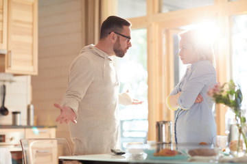 Fototapeta na wymiar Young married Caucasian couple arguing about household duties while standing in home kitchen illuminated with bright morning sun