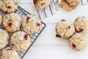 Fresh cranberry muffins cooling on a bakers rack over a rustic white table background. Image shot from above with free space for text.