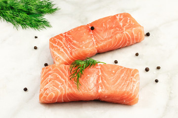 A photo of two slices of salmon on a white marble kitchen table with salt, pepper, and herbs