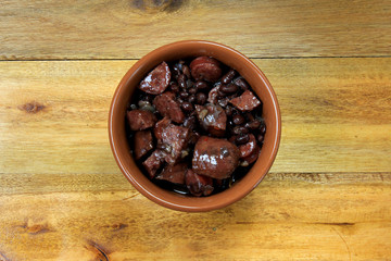pot with feijoada, traditional brazilian cuisine dish, isolated under wooden background, top view