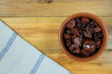 pot with feijoada, traditional brazilian cuisine dish, isolated under wooden background, top view