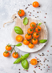 Organic Cherry Orange Rapture Tomatoes on the Vine with basil and pepper on chopping board on stone kitchen background.